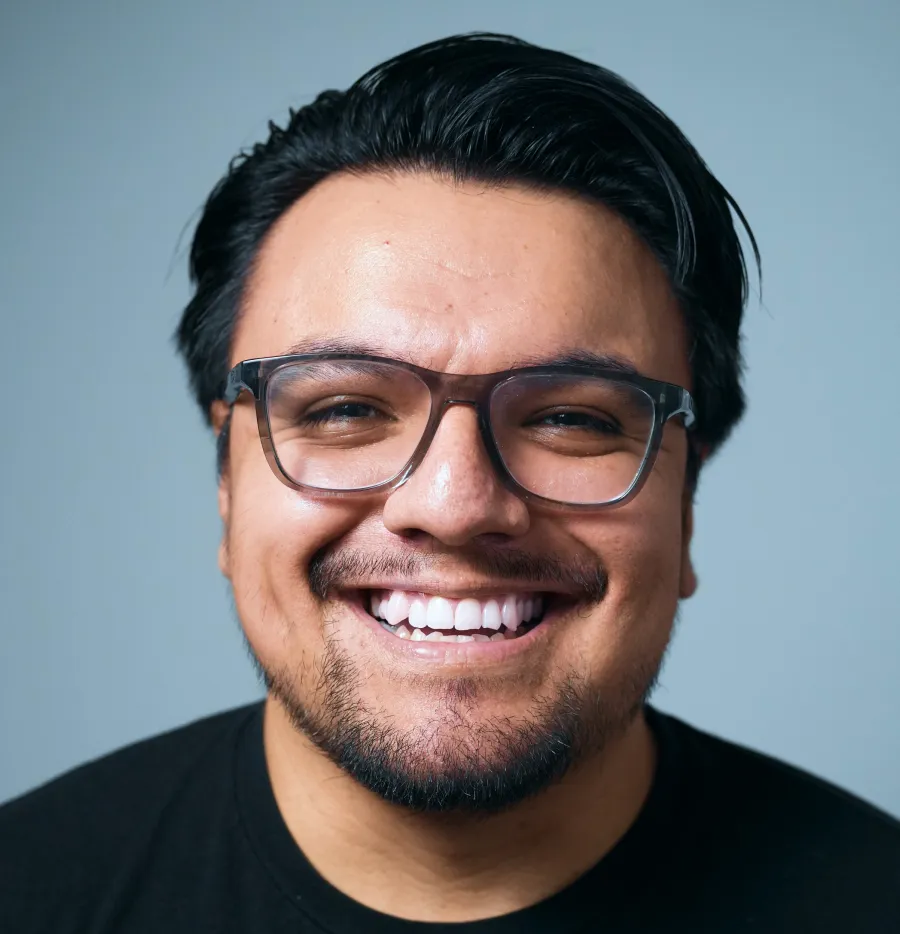 Andrés Flores qui sourit, lunettes et t-shirt noir, sur un fond gris.